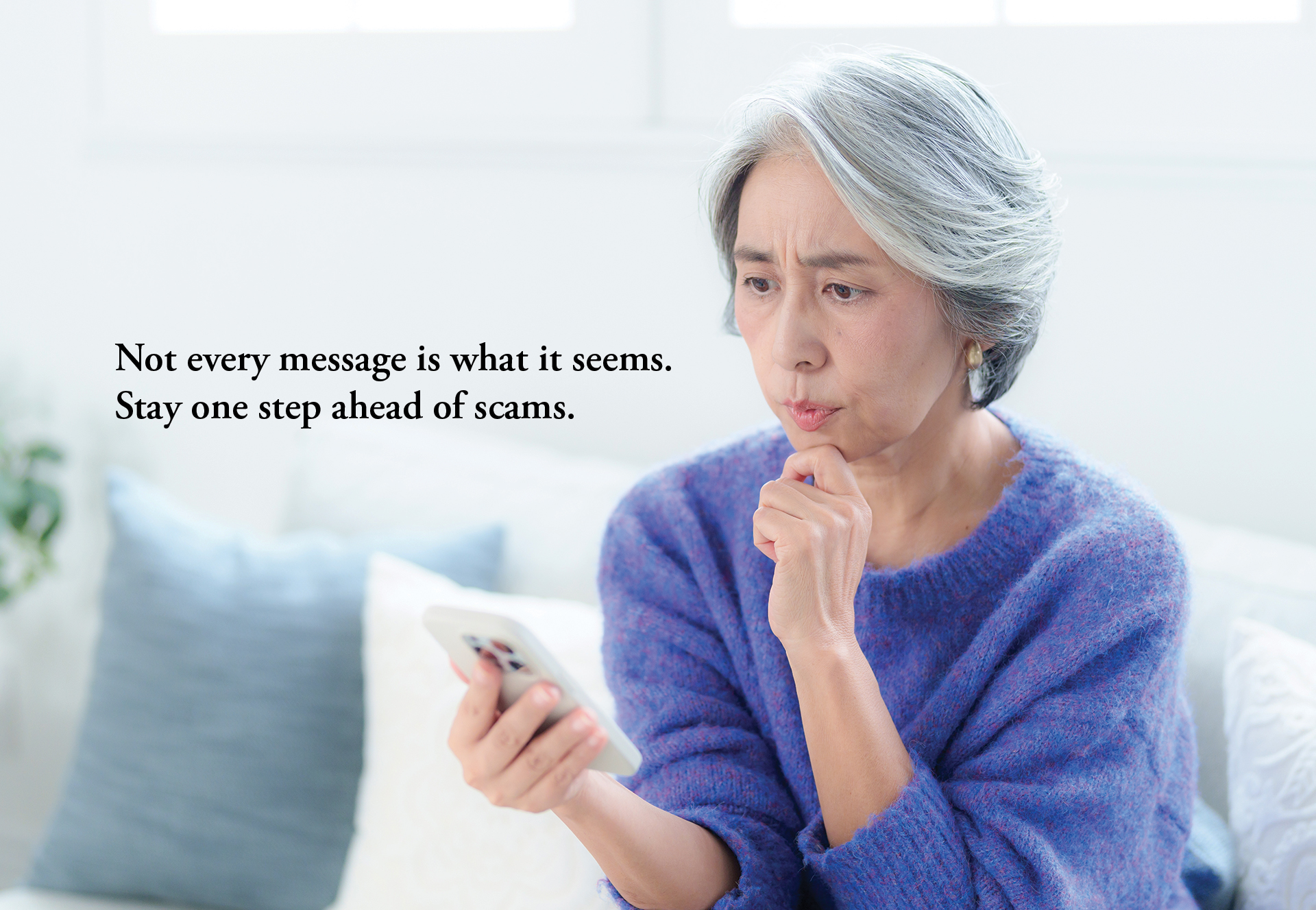 Unsure, mature Asian woman with looking at smart phone. Text on image says 'Not every message is what it seems. Stay one step ahead of scams.'