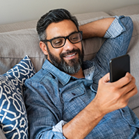 Smiling Hispanic man with glasses using smart phone