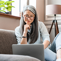 Middle aged Asian woman sitting on couch looking at laptop