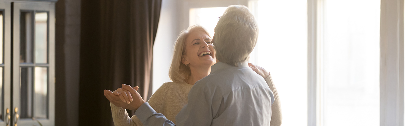 Dancing couple in living room in front of window.